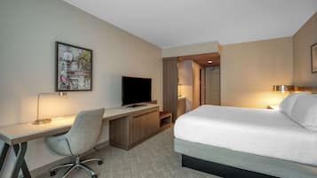 Quarto de hotel com cama, escrivaninha, cadeira, televisão e um quadro na parede.