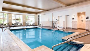 An indoor swimming pool with clear water, tiled edges, and a pool lift. There are lounge chairs and a sunshade area with umbrellas. - Hilton Garden Inn Boston Logan Airport (Boston)