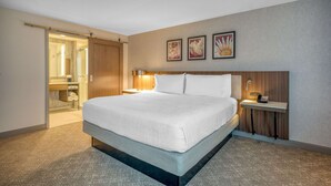 A hotel room with a large bed, a bedside table with a lamp, a wooden headboard, and a small desk with a telephone. - Hilton Garden Inn Boston Logan Airport (Boston)