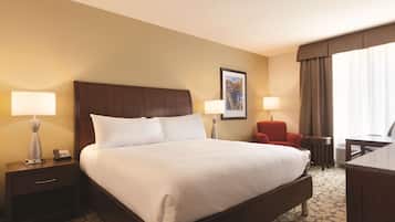 A hotel room with a large bed, two bedside tables with lamps, a red chair, a desk, and a framed picture on the wall.