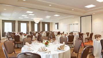 A large conference room with multiple round tables set for dining, equipped with chairs, table settings, and a chandelier.