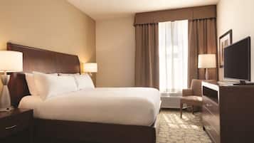 A hotel room with a large bed, two bedside lamps, a flat-screen TV, a desk with a chair, and a window with curtains.