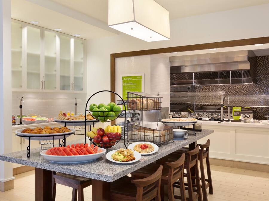 A breakfast buffet with various food items and a kitchen area in the background.