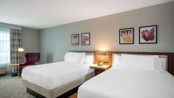 Habitación de hotel con dos camas, una silla, un escritorio con lámpara y cuadros con motivos florales en la pared.