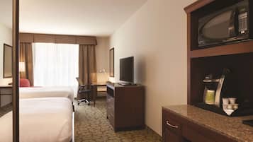 A hotel room with two beds, a desk with a chair, a television, a microwave, and a coffee maker.