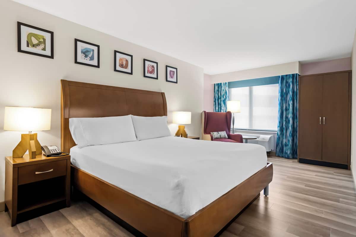 A hotel room with a large bed, bedside lamps, a desk with a chair, a wardrobe, and framed pictures on the wall.