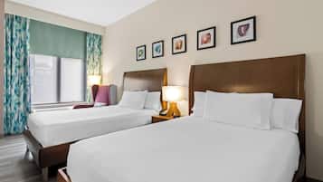 A hotel room with two beds, a window with curtains, a lamp, and framed pictures on the wall.