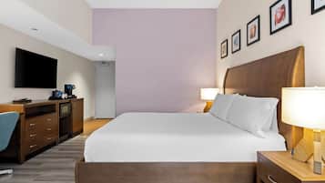 A hotel room with a bed, bedside table, lamp, desk with a computer, and a TV.