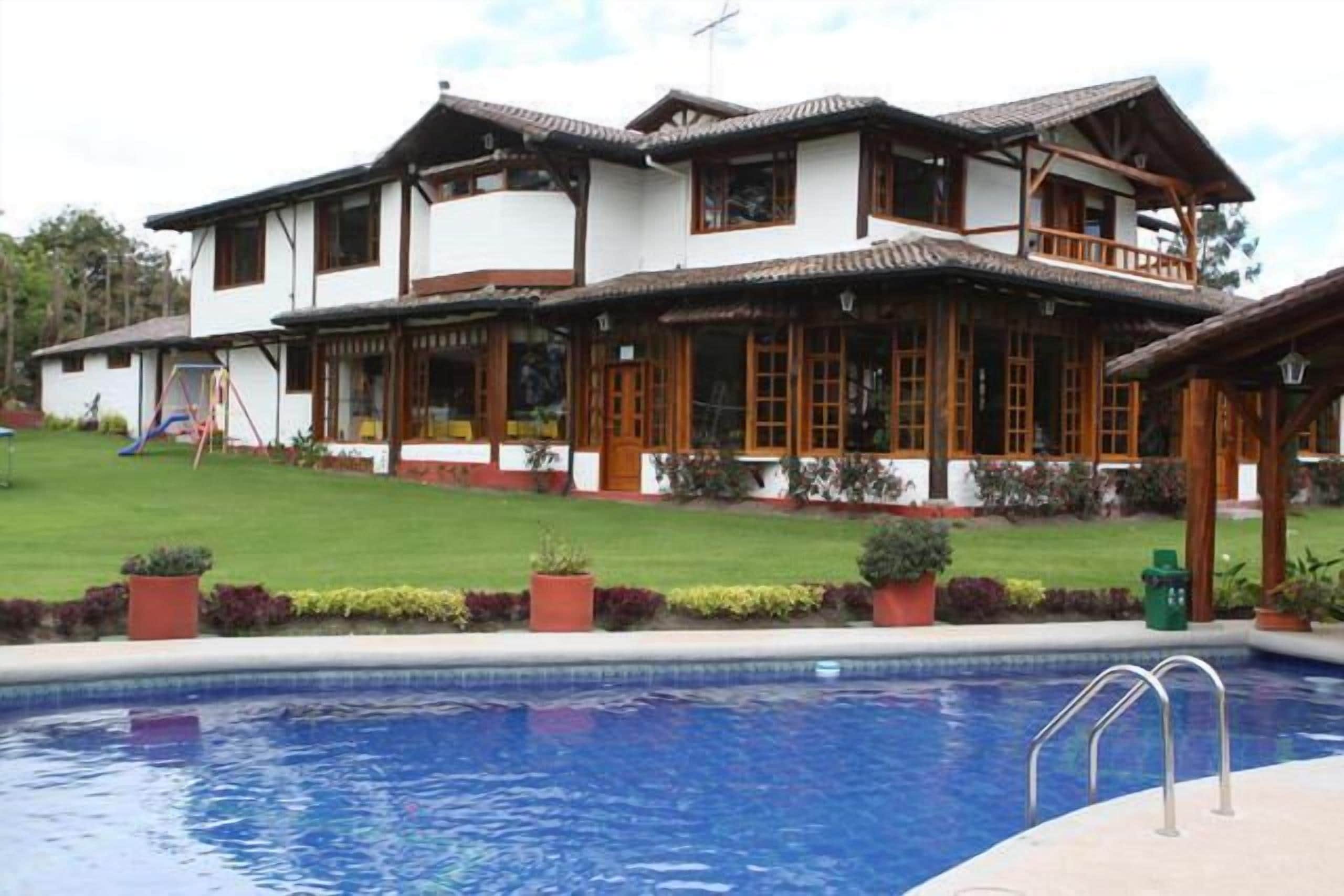 A two-story house with a balcony, a swimming pool, and a well-maintained lawn.