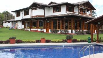 A two-story house with a balcony, a swimming pool, and a well-maintained lawn.
