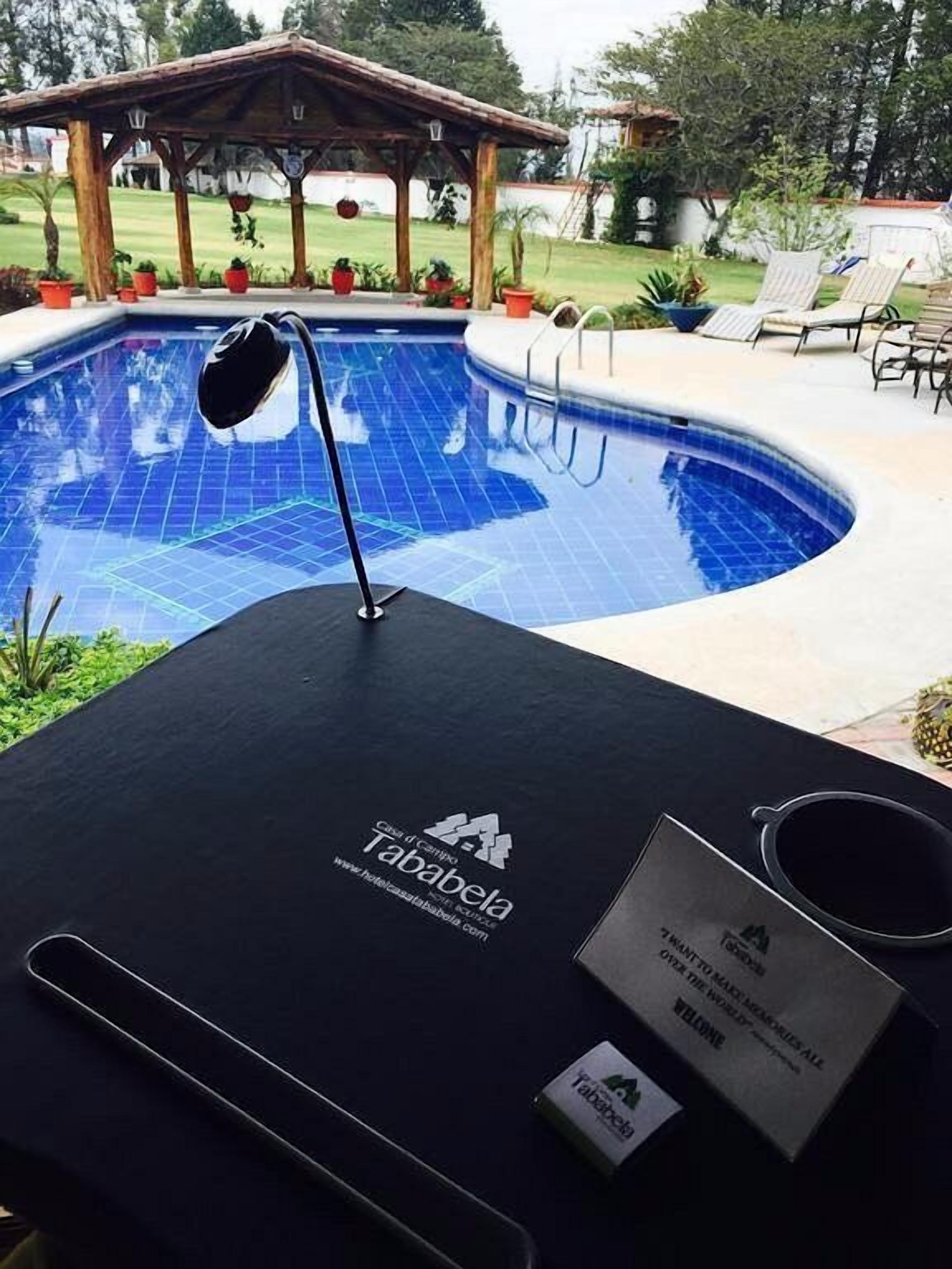 A poolside area with a wooden pergola, lounge chairs, and a sign for 'Tababela'.
