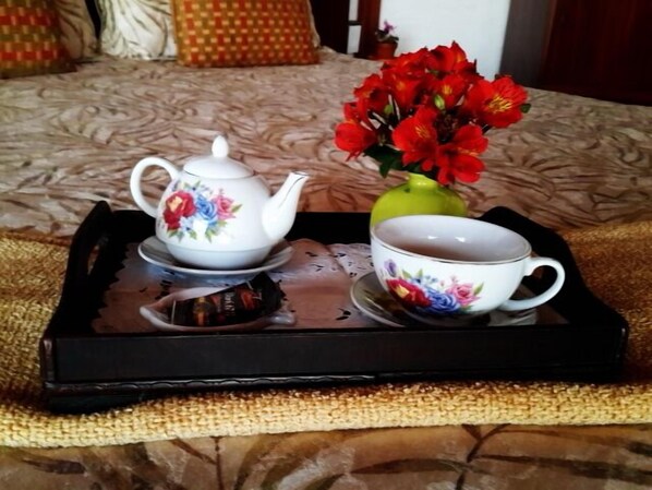 A tray with a teapot, a cup, and a vase of red flowers on a textured surface.