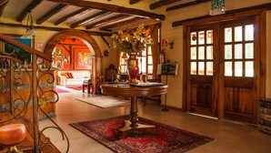 Un hall d’entrée avec une table ronde en bois, un tapis rouge à motifs et une porte en bois dotée de fenêtres.
