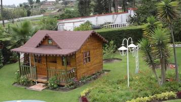 A wooden cabin with a porch, surrounded by a garden with various plants and flowers.