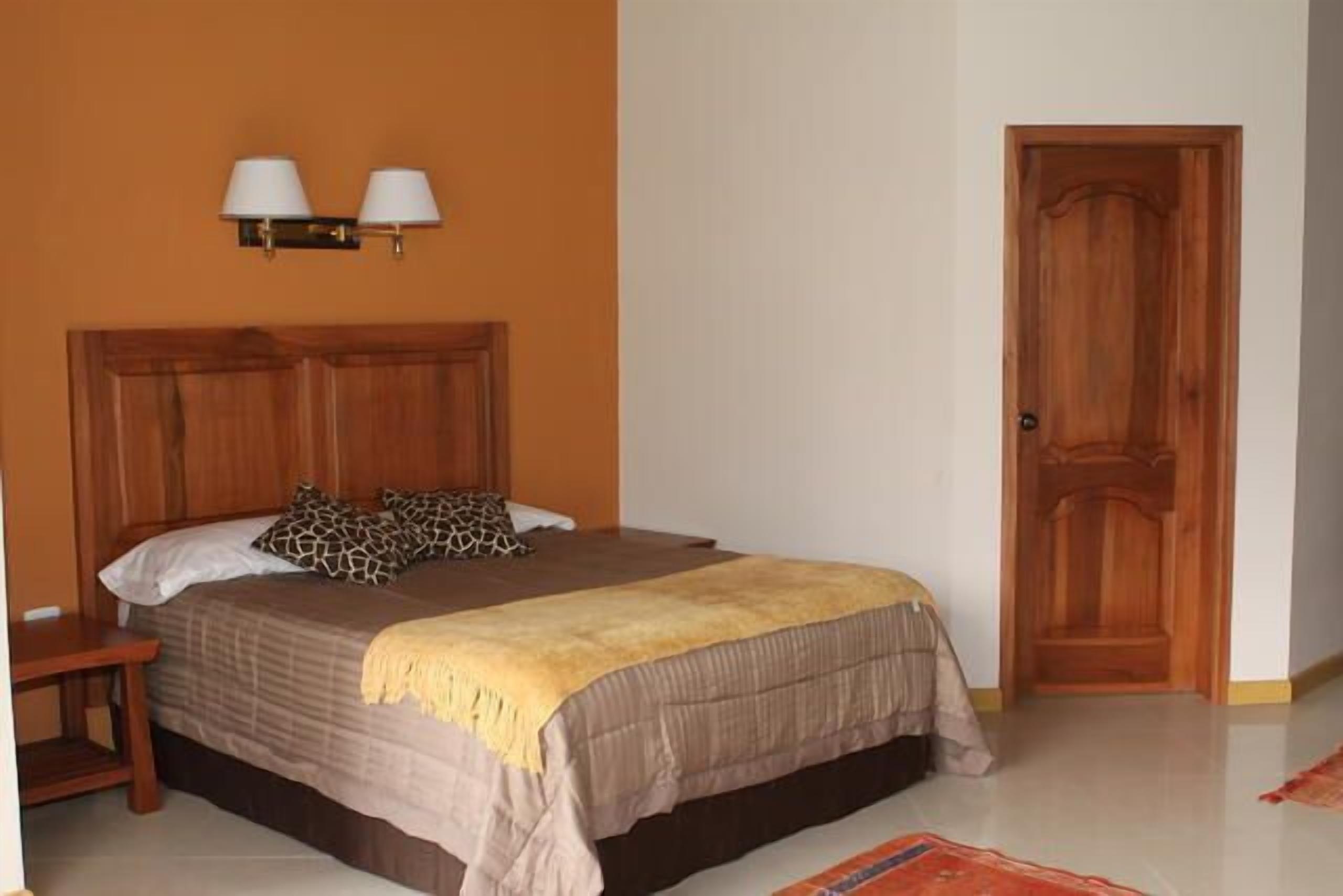 Un dormitorio con cabecera de madera, una cama con almohadas estampadas, una mesita de noche y una puerta.