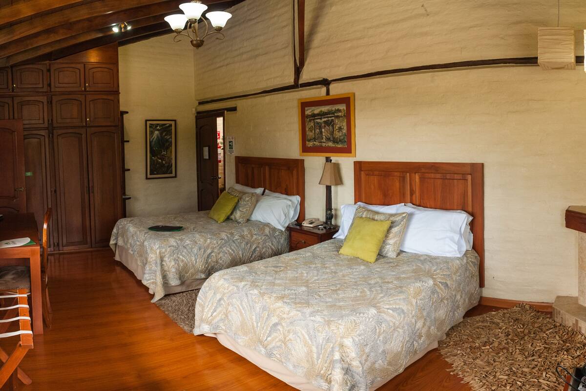 Ein Zimmer mit zwei Betten, Holzmöbeln, einem Schreibtisch und einem Kamin.