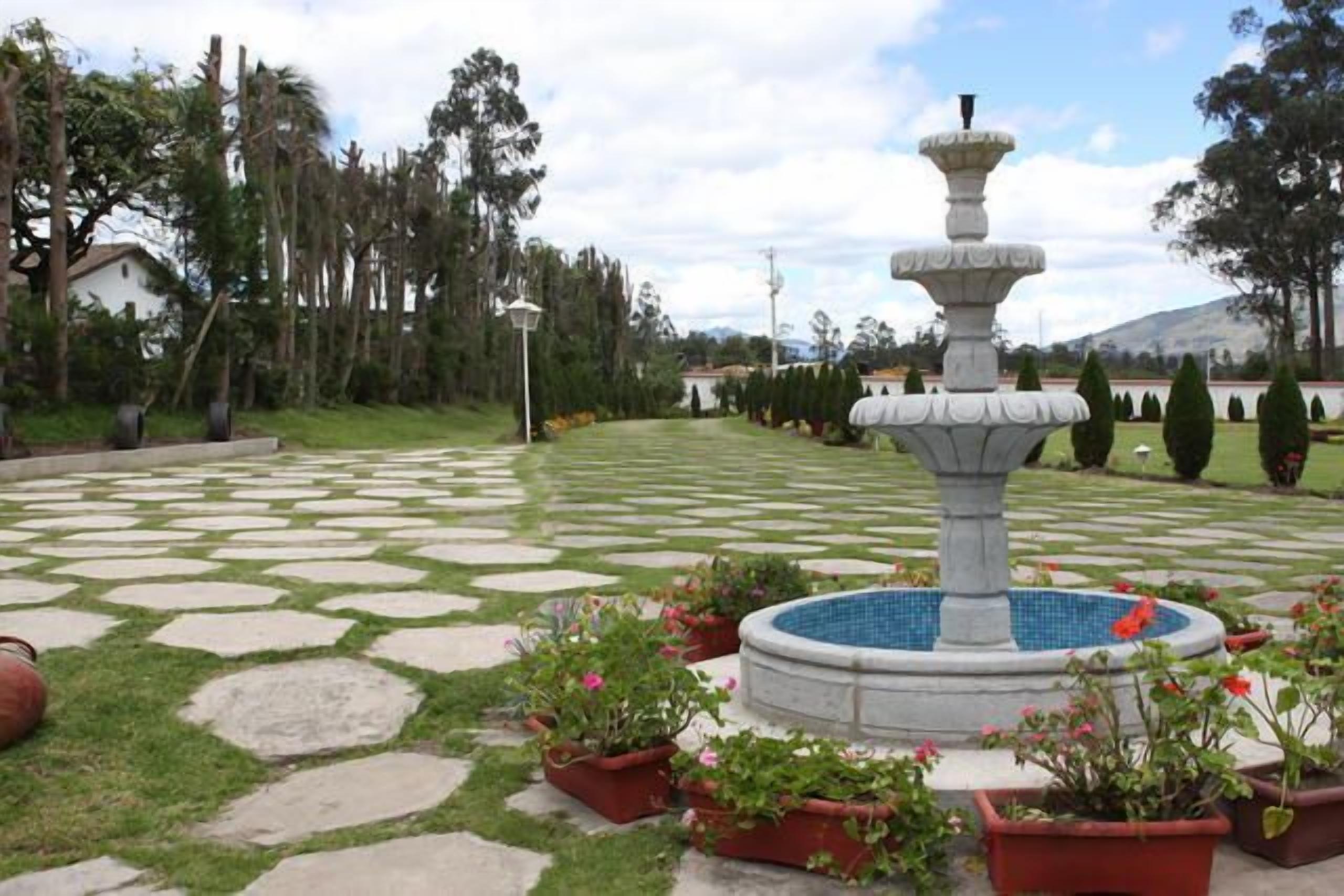 Un jardín con una fuente, baldosas de piedra y plantas en macetas.