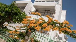 A modern white building with balconies and orange flowering plants in front. - Kardamena Holiday Apartments (Kos)