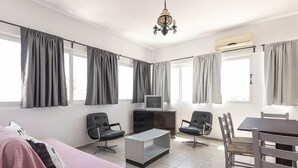 A modern living room with a sofa, chairs, a TV, and a dining table. - Kardamena Holiday Apartments (Kos)