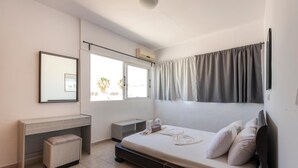 A modern bedroom with a bed, a desk, a chair, and a window. - Kardamena Holiday Apartments (Kos)