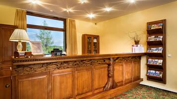 A wooden reception desk with a lamp, a bulletin board, and a bookshelf with brochures.