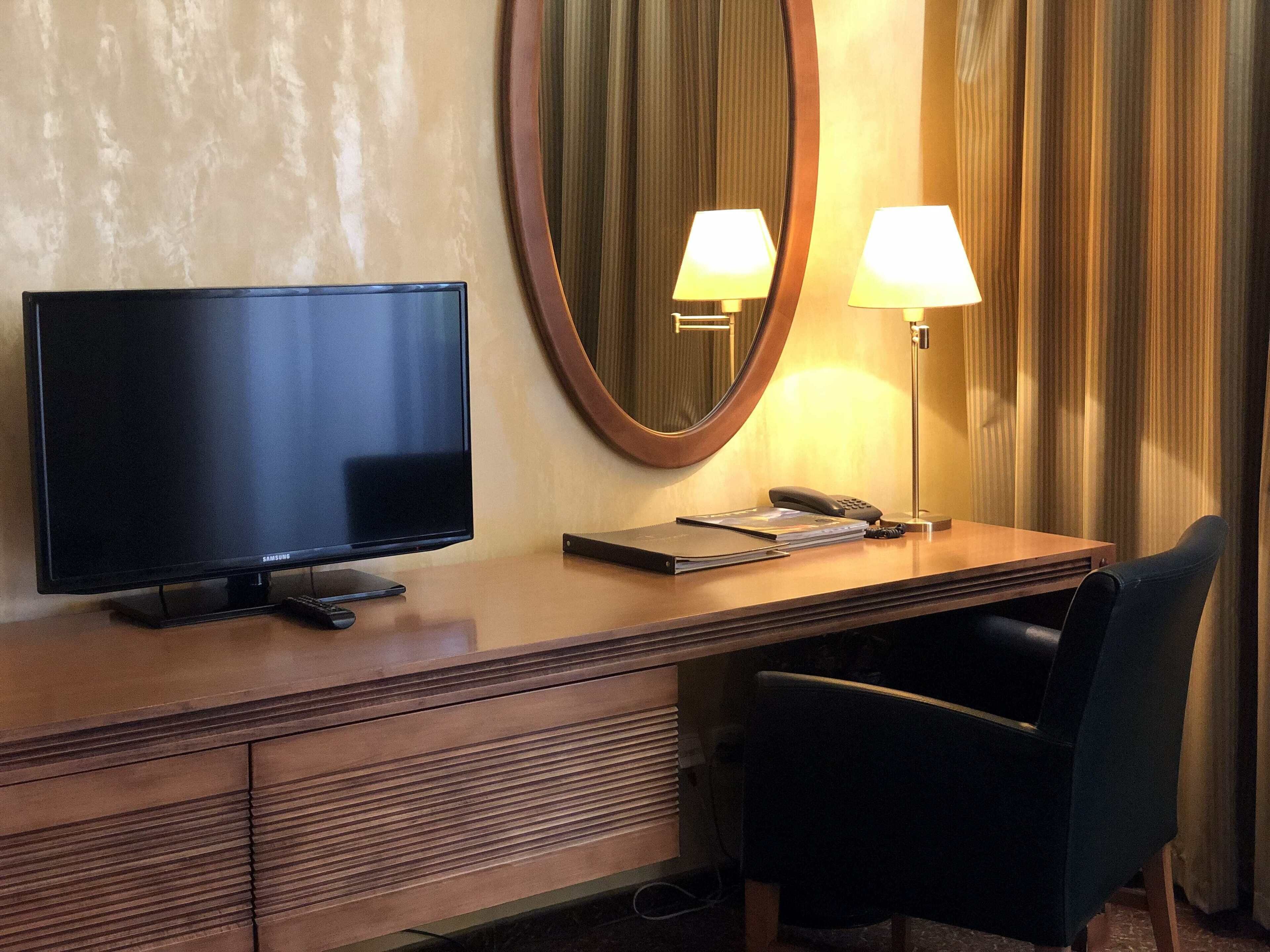 Ein Hotelzimmer mit Flachbildfernseher, Schreibtisch mit Lampe, Telefon und Stuhl.