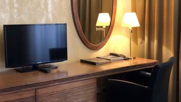 Ein Hotelzimmer mit Flachbildfernseher, Schreibtisch mit Lampe, Telefon und Stuhl.