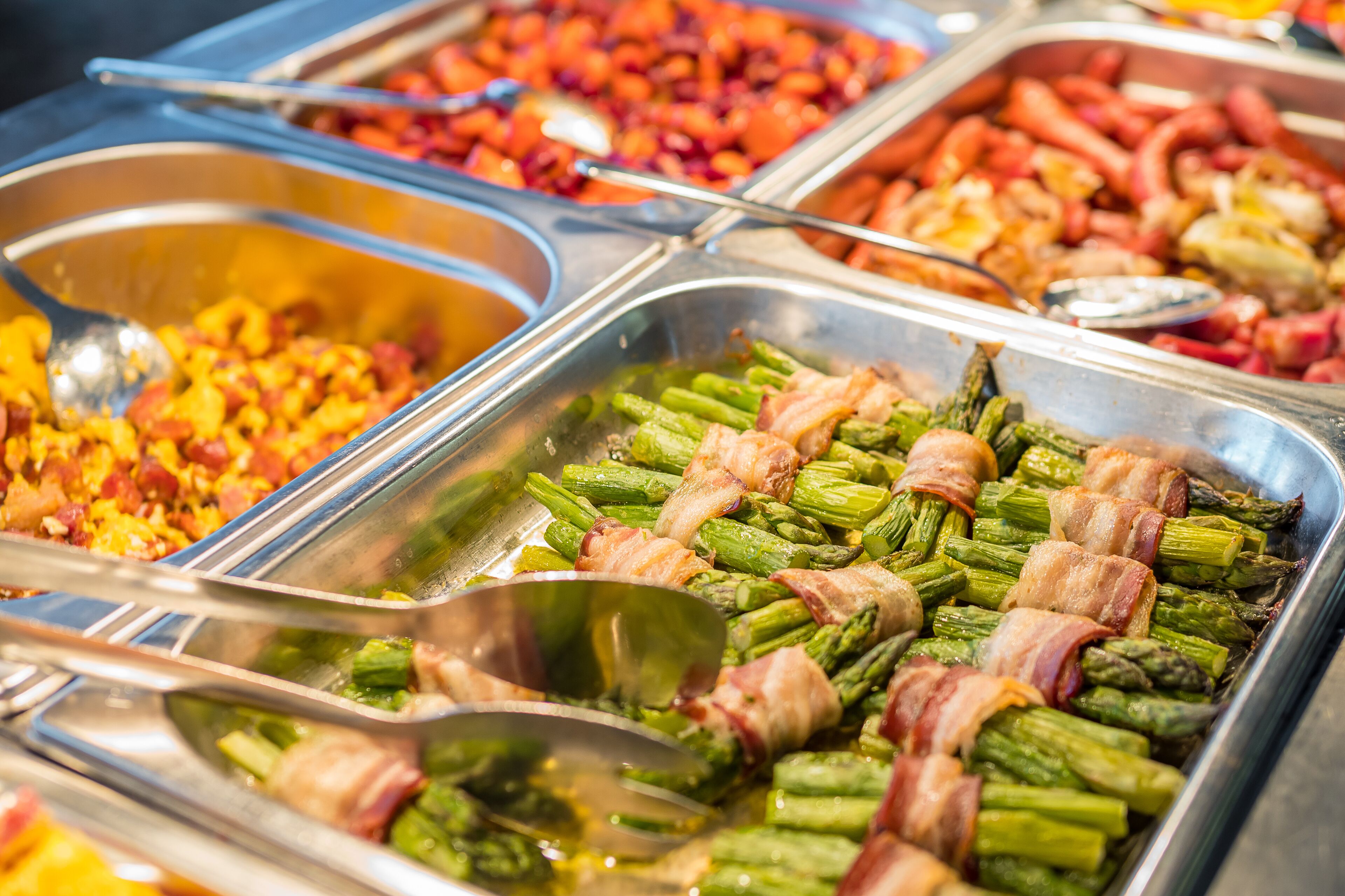 Un buffet proposant divers plats, notamment des asperges enroulées de lardons et d’autres légumes variés.