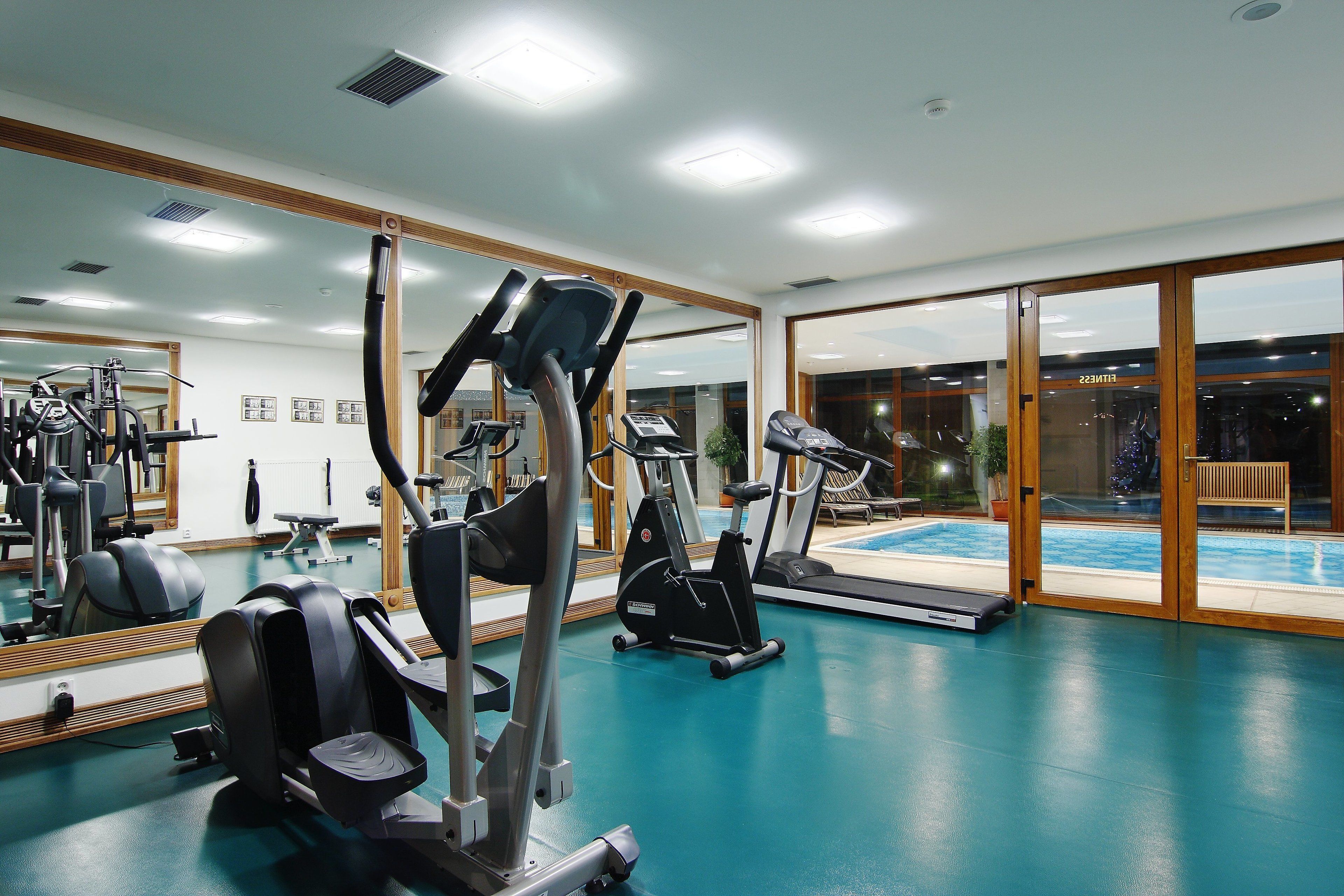 A gym with exercise equipment, a large mirror, and a view of a swimming pool.