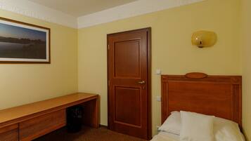 Habitación de hotel con una cama de madera, un banco, una puerta y un aplique en la pared.