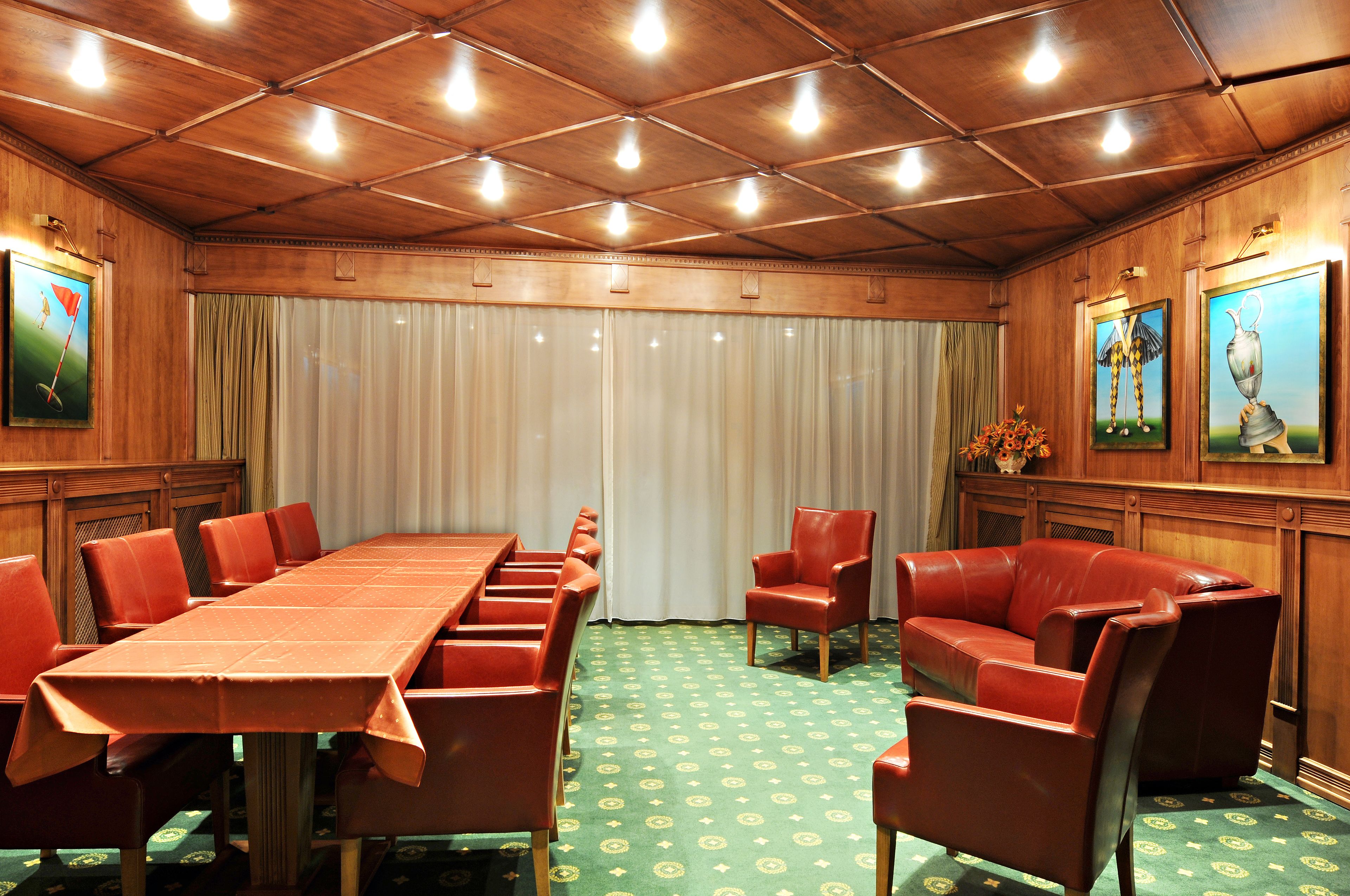 A conference room with a long table, red chairs, a leather sofa, and wooden paneling.