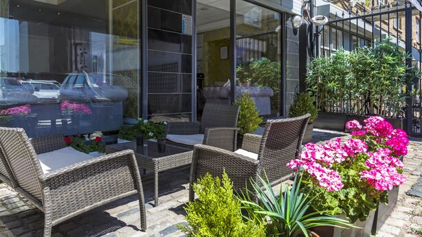 An outdoor seating area with wicker furniture and potted plants. - Hotel Shepherds Bush London (London)