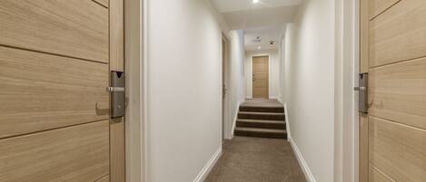 A hallway with wooden paneling on the walls, carpeted floor, and a staircase leading to another room.
