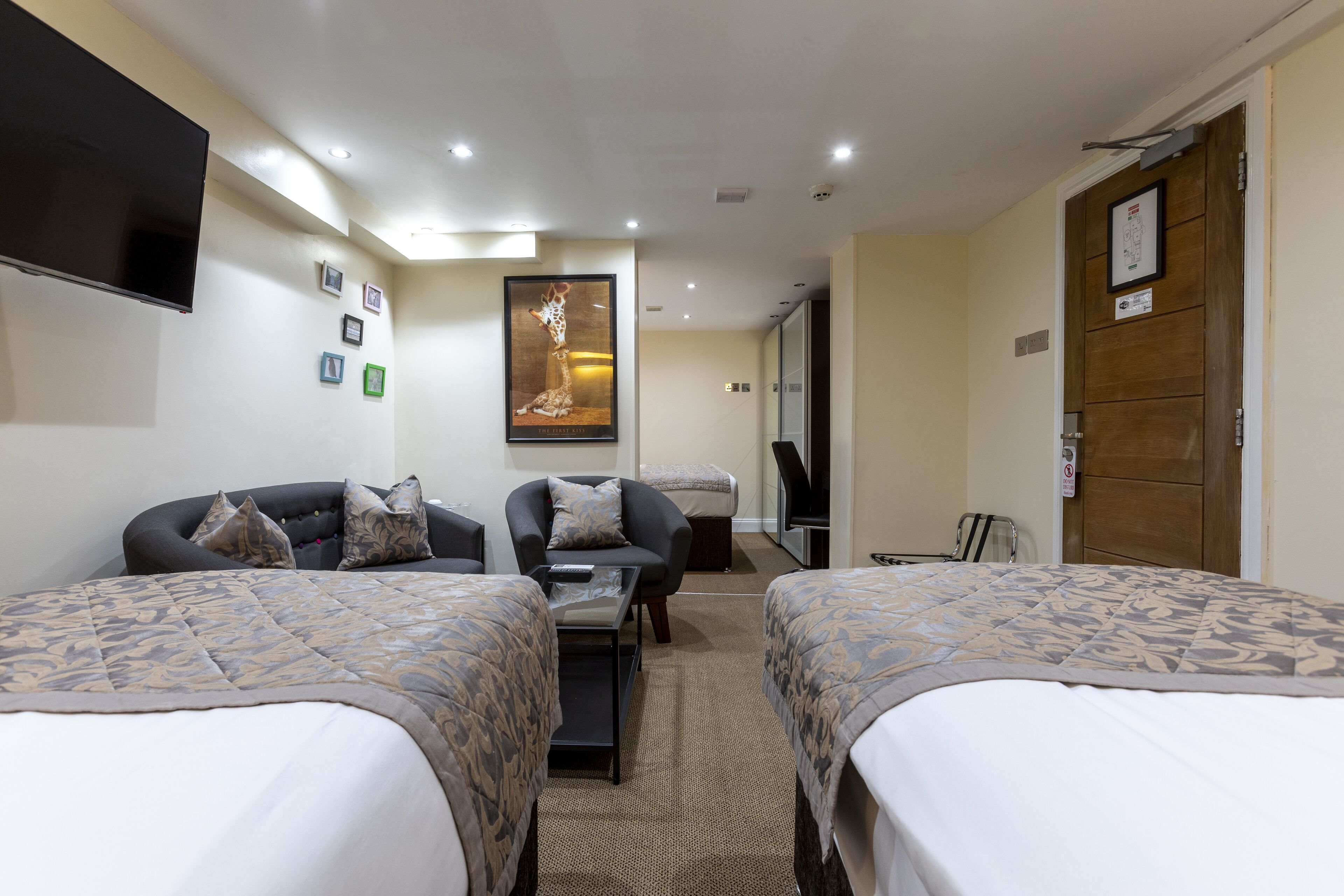 A hotel room with two beds, a sofa, a TV, and a framed picture on the wall.
