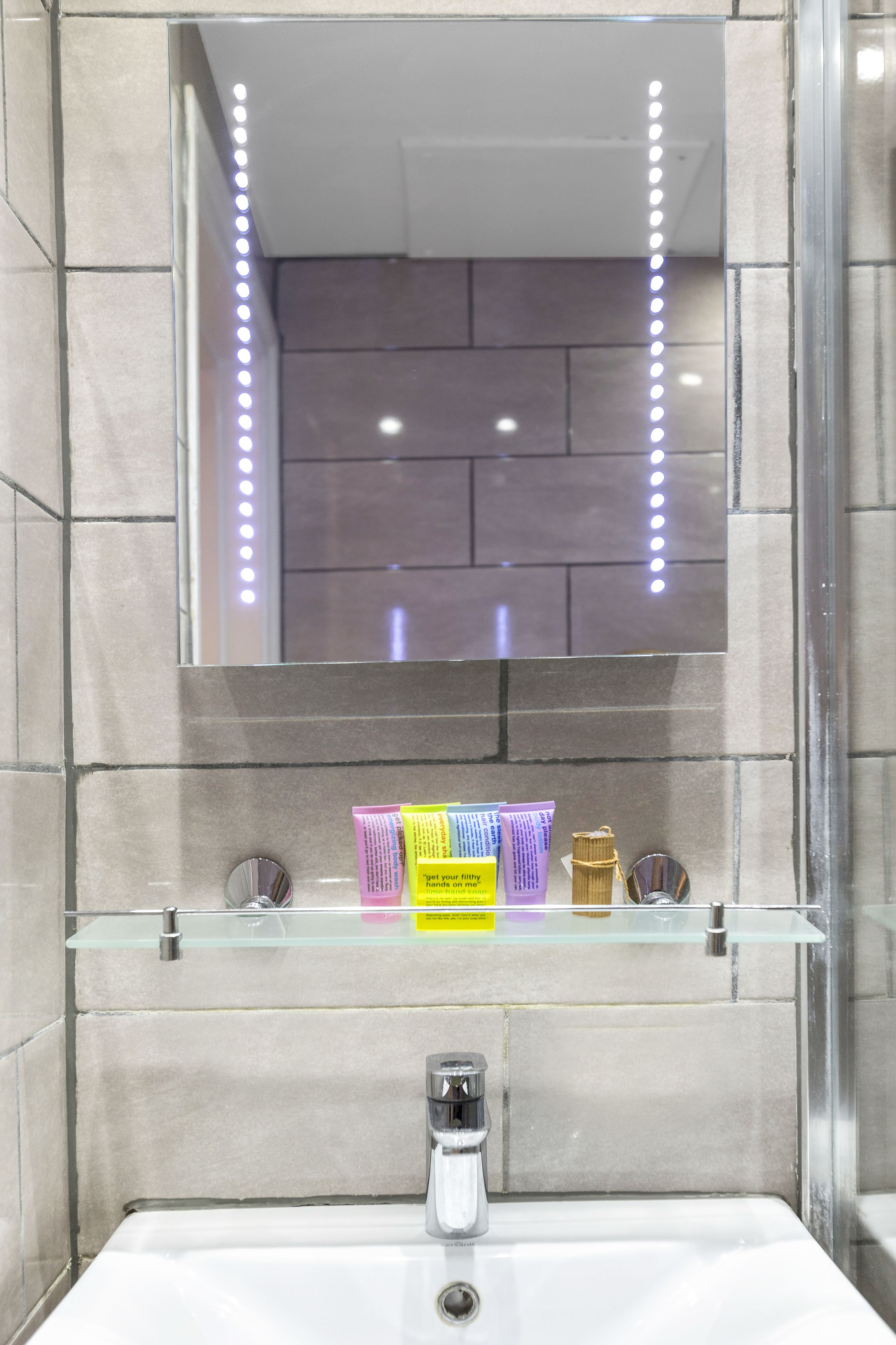 A modern bathroom with a glass shelf holding toiletries, a mirror with LED lights, and a sink with a faucet.