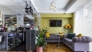 A modern living room with a bar area, a sofa, a coffee table, and a potted plant. - Hotel Shepherds Bush London (London)