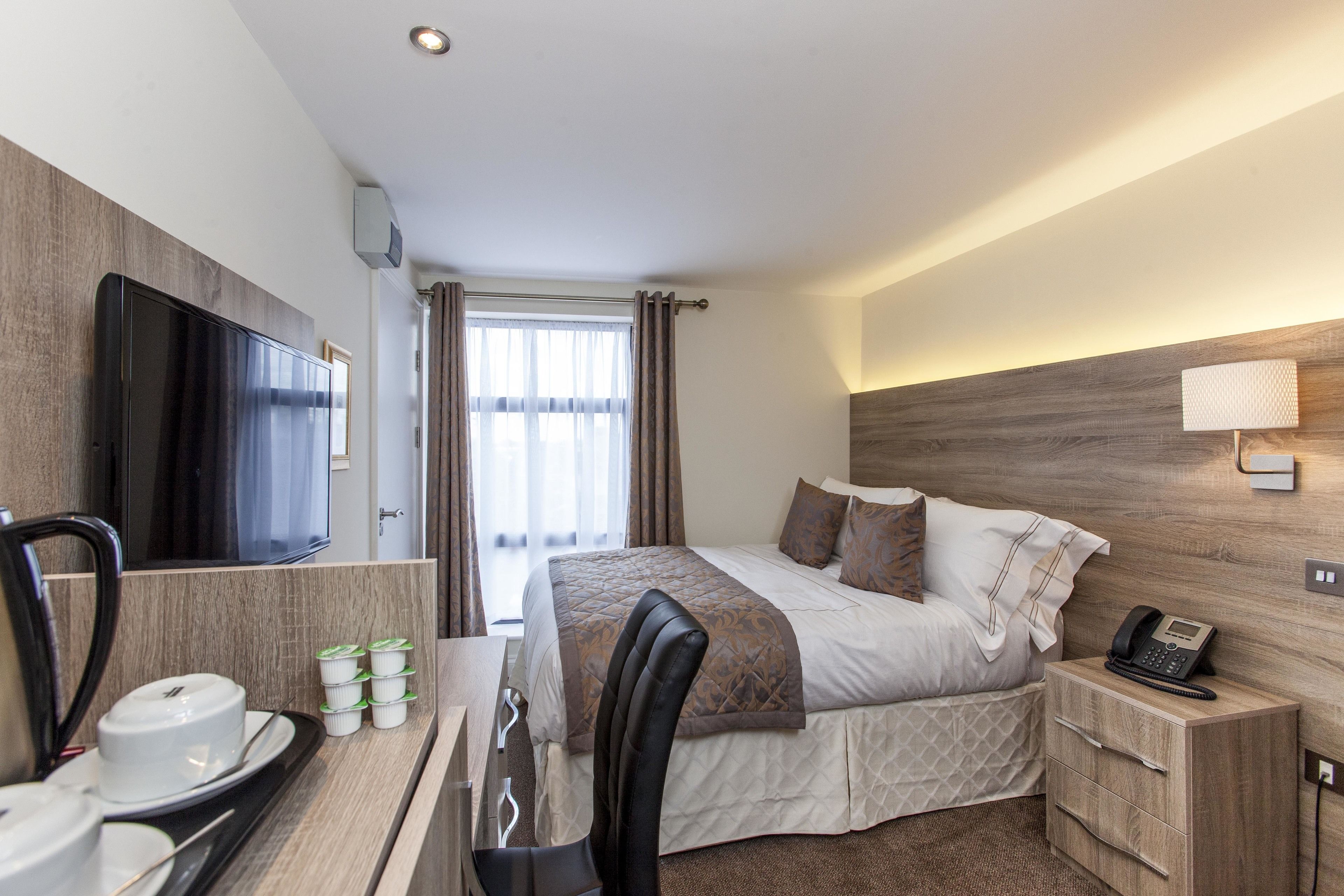 A hotel room with a bed, bedside table, lamp, and a TV mounted on the wall.