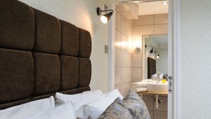 A bedroom with a large headboard, a bedside table, and a bathroom visible through an open door. - Hotel Shepherds Bush London (London)