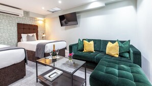 A hotel room with a bed, a green sofa, a coffee table, and a flat-screen TV mounted on the wall. - Hotel Shepherds Bush London (London)