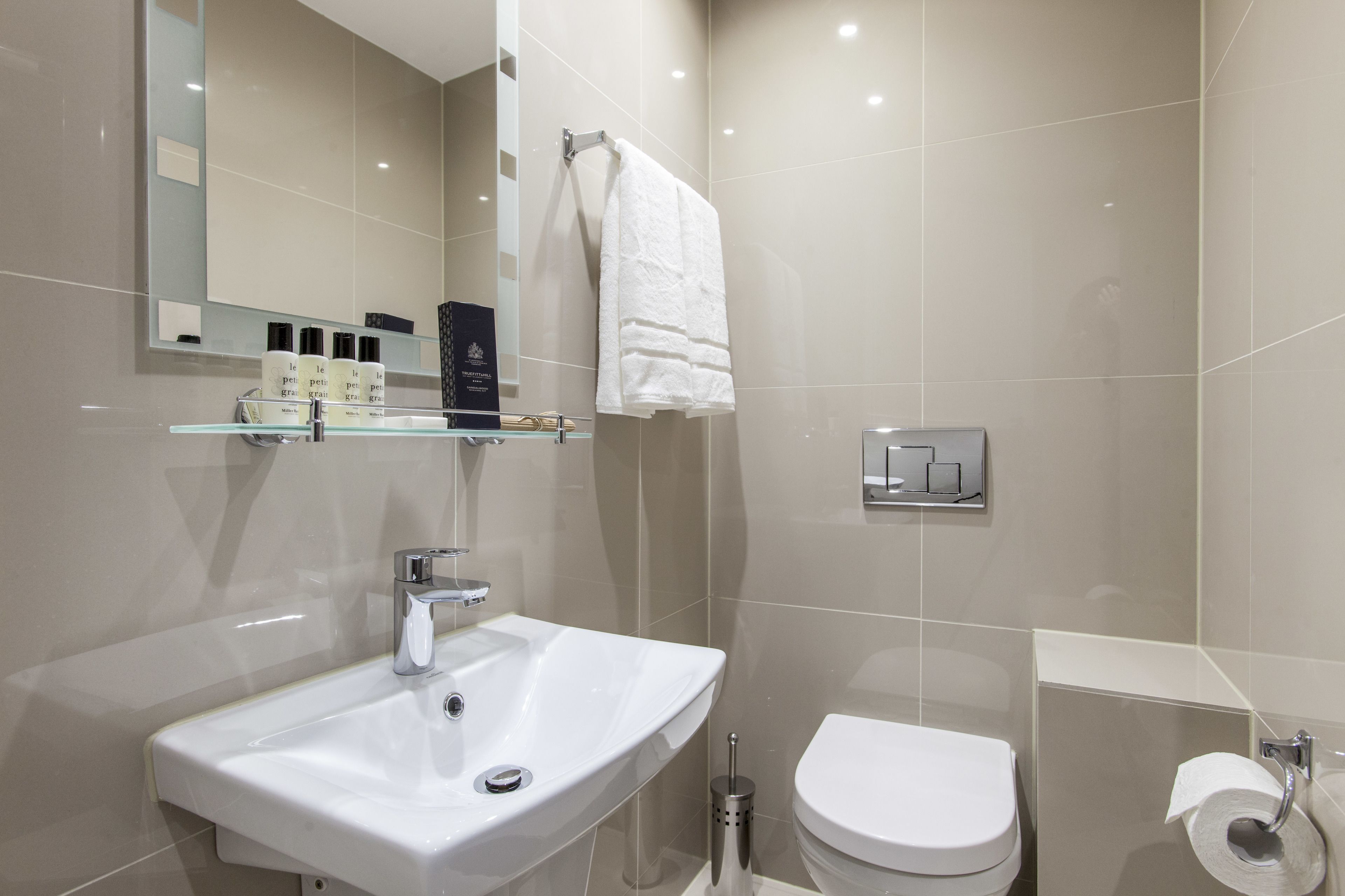 A modern bathroom with a white sink, a toilet, and a glass shelf with toiletries.