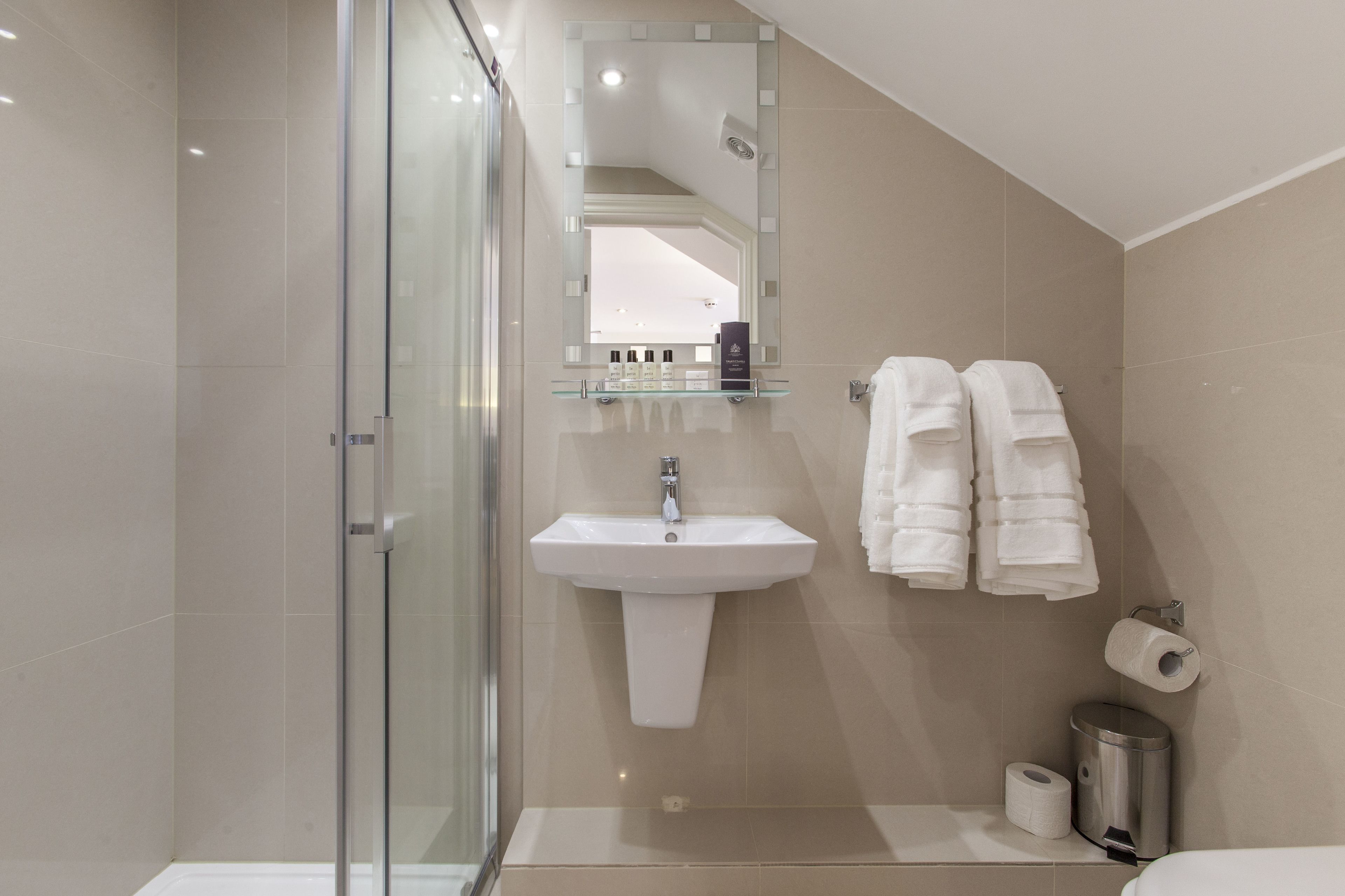 A modern bathroom with a glass shower enclosure, a pedestal sink, and a mirror with a shelf above it.