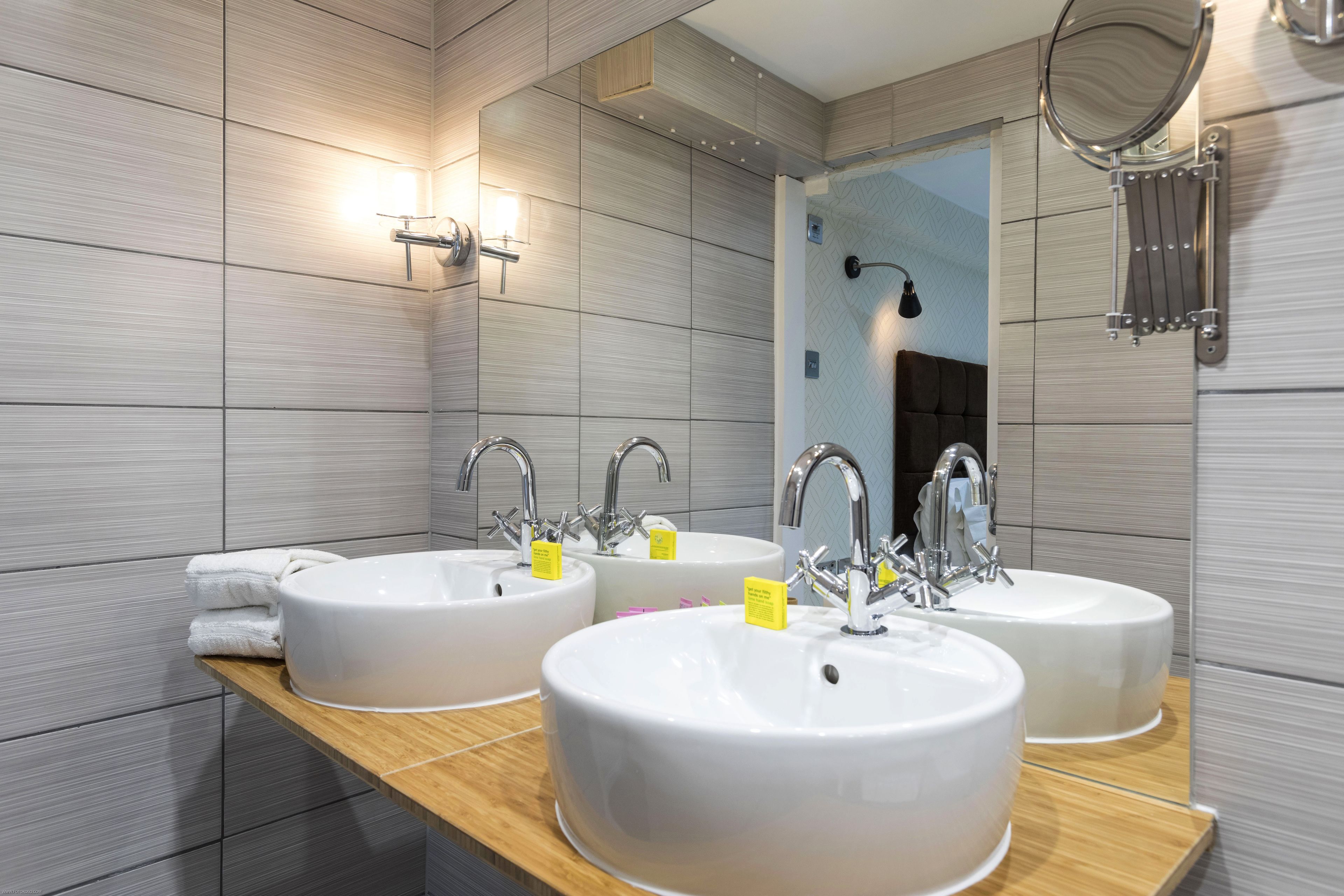 A modern bathroom with three sinks, a wooden vanity, and a large mirror.