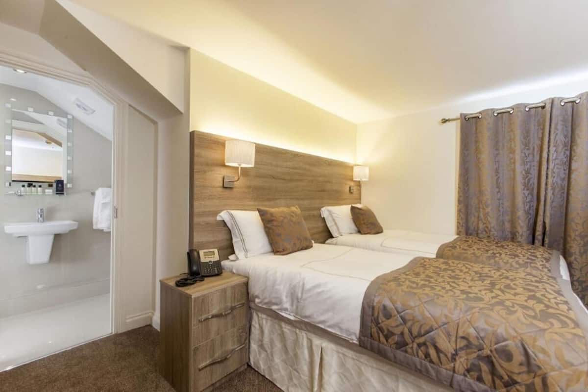 A hotel room with a bed, bedside table, lamp, and a bathroom with a sink and mirror.