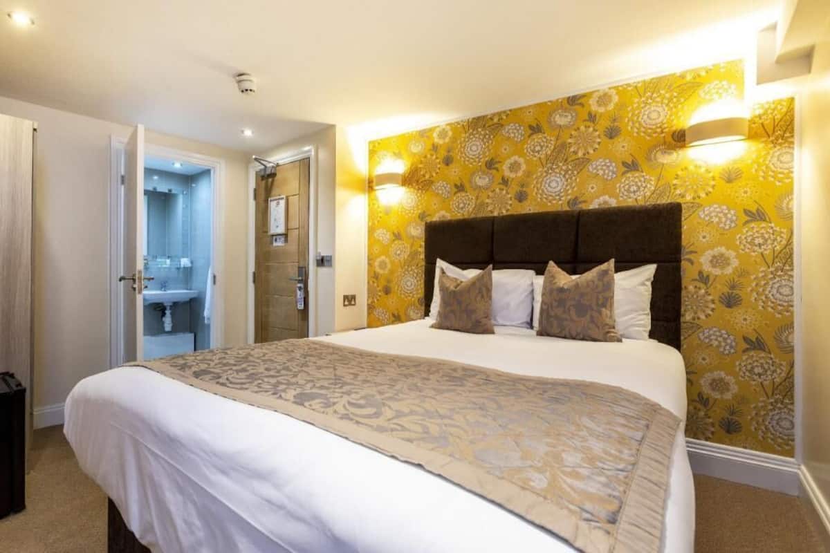 A hotel room with a large bed, a bathroom with a sink and mirror, and a door leading to another room.