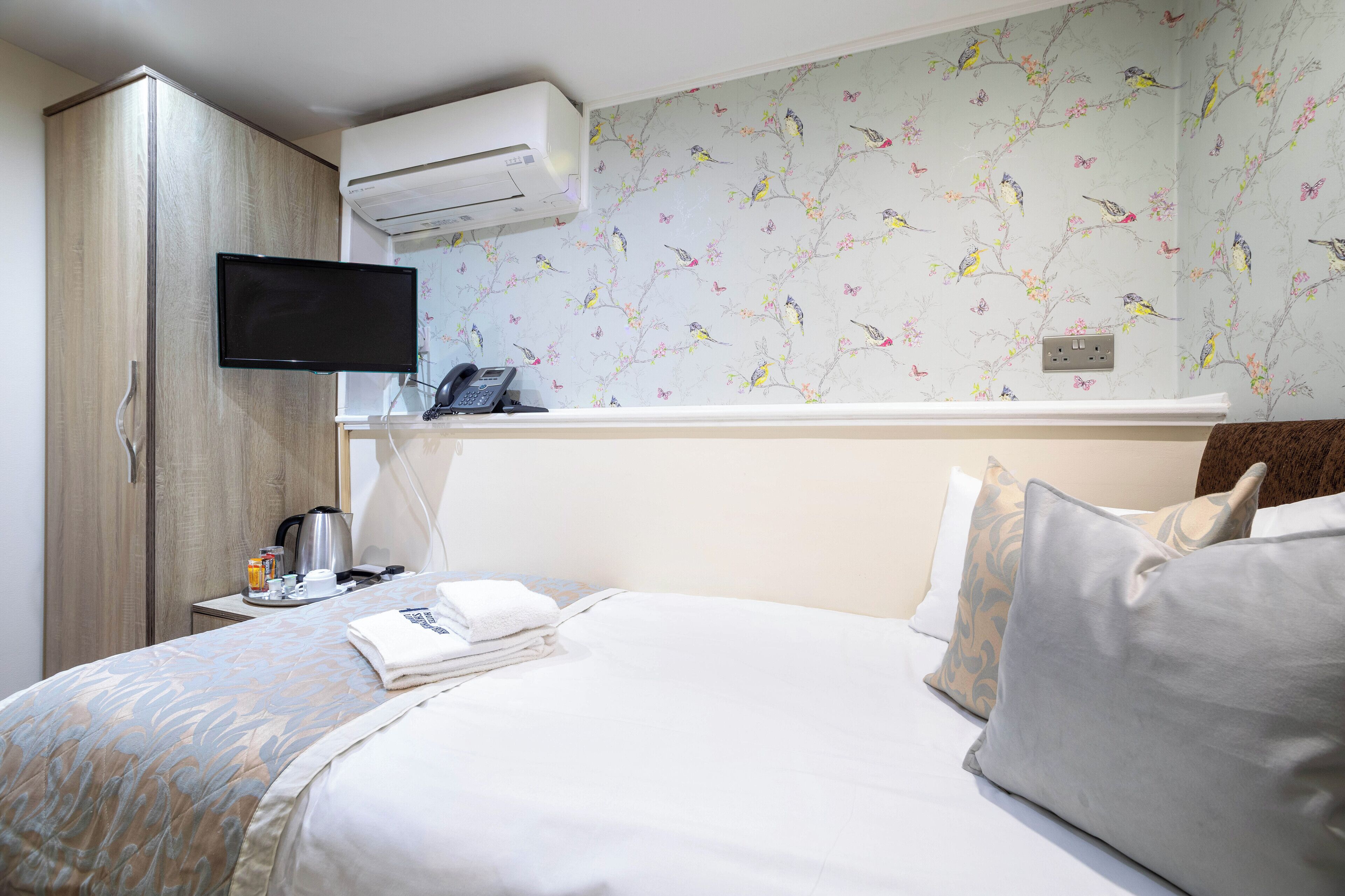 Una habitación de hotel con una cama, un televisor montado en la pared, un armario y una mesita con cafetera y teléfono.