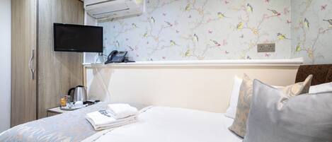Una habitación de hotel con una cama, un televisor montado en la pared, un armario y una mesita con cafetera y teléfono.