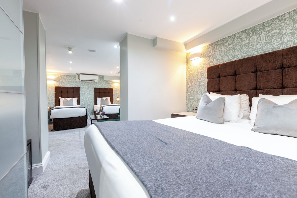 A modern hotel room with a large bed, a separate seating area, and a bathroom with a mirror and vanity.