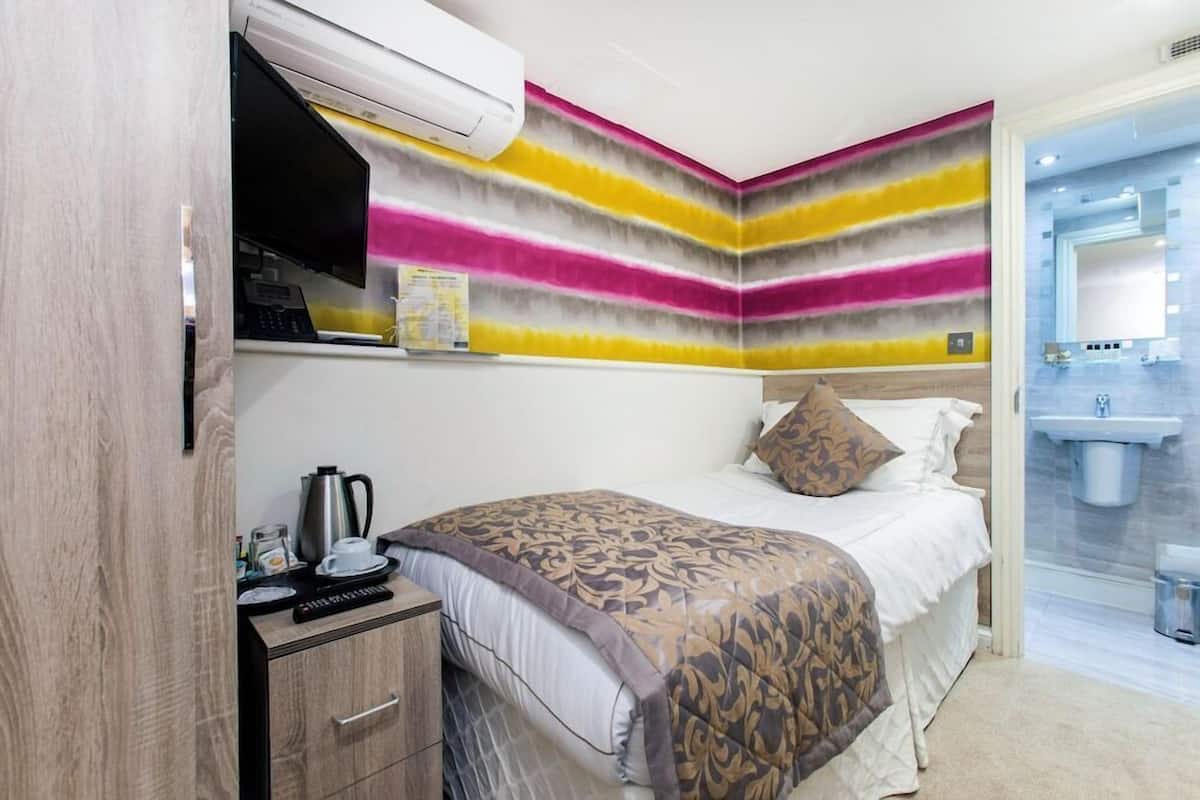 A hotel room with a bed, bedside table, and a bathroom with a sink and mirror.