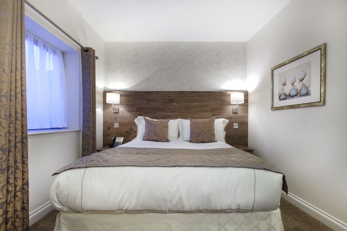 A neatly made bed with a patterned bedspread, a wooden headboard, and a wall-mounted lamp.