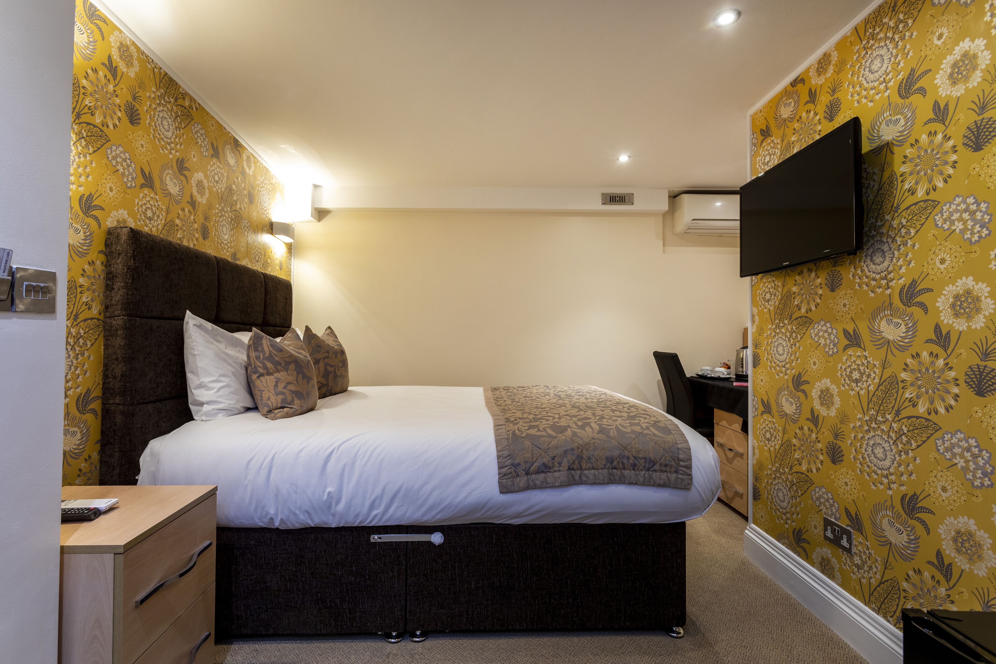 A bedroom with a bed, bedside table, and a mounted TV.